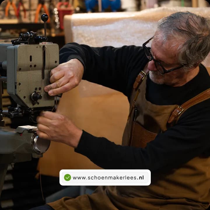 Schoenmaker met bril en leren schort aan het werk achter een naaimachine in zijn werkplaats, met een groen vinkje bij de domeinnaam www.schoenmakerlees.nl.