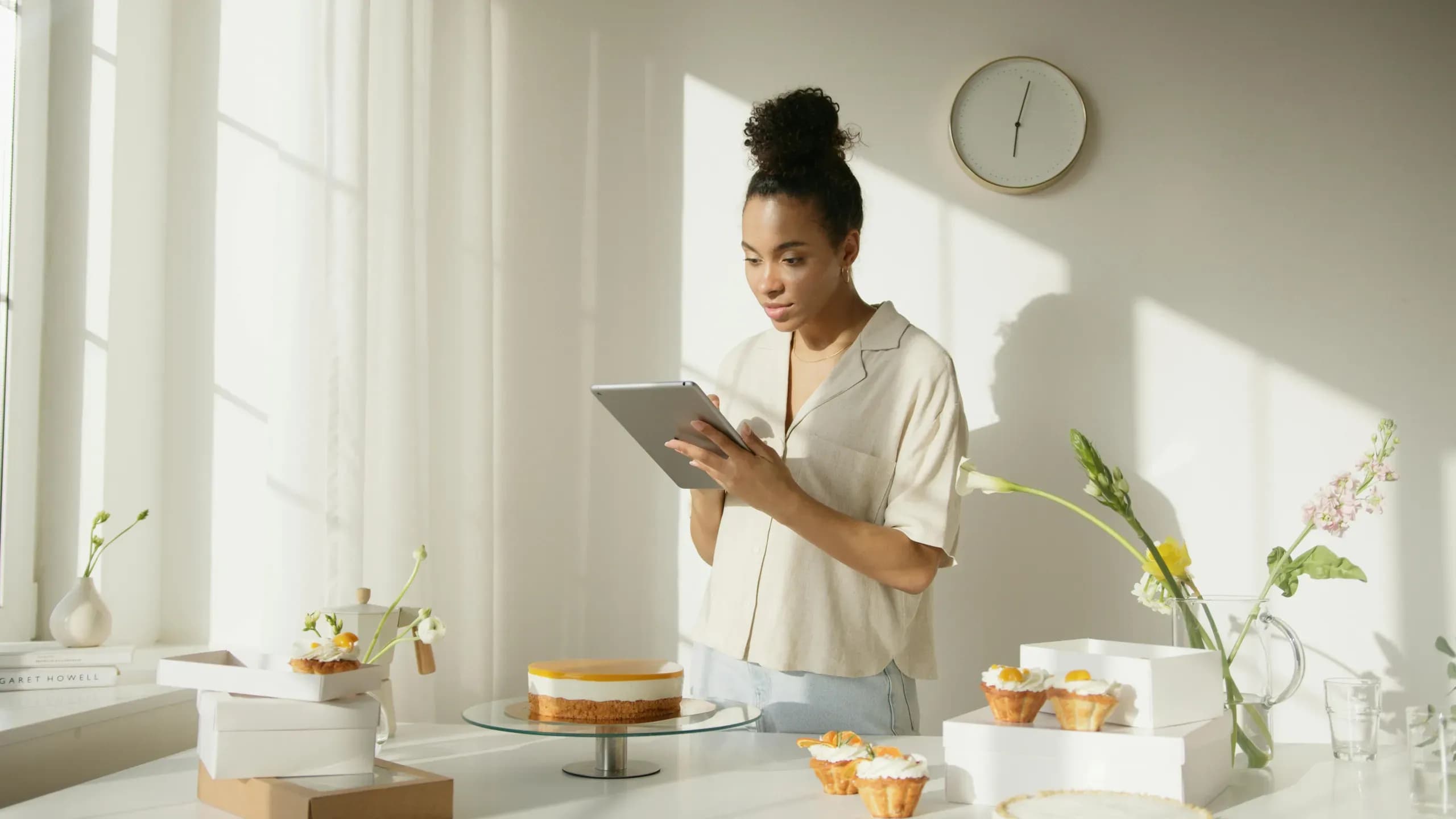 Een vrouw die in de keuken staat met haar baksels, en tegelijkertijd op haar ipad bezig is met haar onderneming