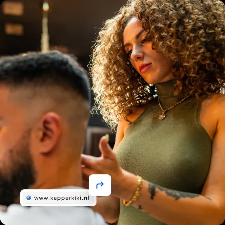 Kapster met krullend haar knipt het haar van een klant, met in beeld de domeinnaam www.kapperkiki.nl en een pijlicoon.