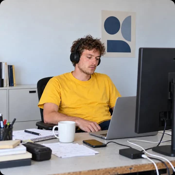 Beeldscherm vol code op een bureau, naast een glimlachende man met een blauwe Hostnet-koffiemok.