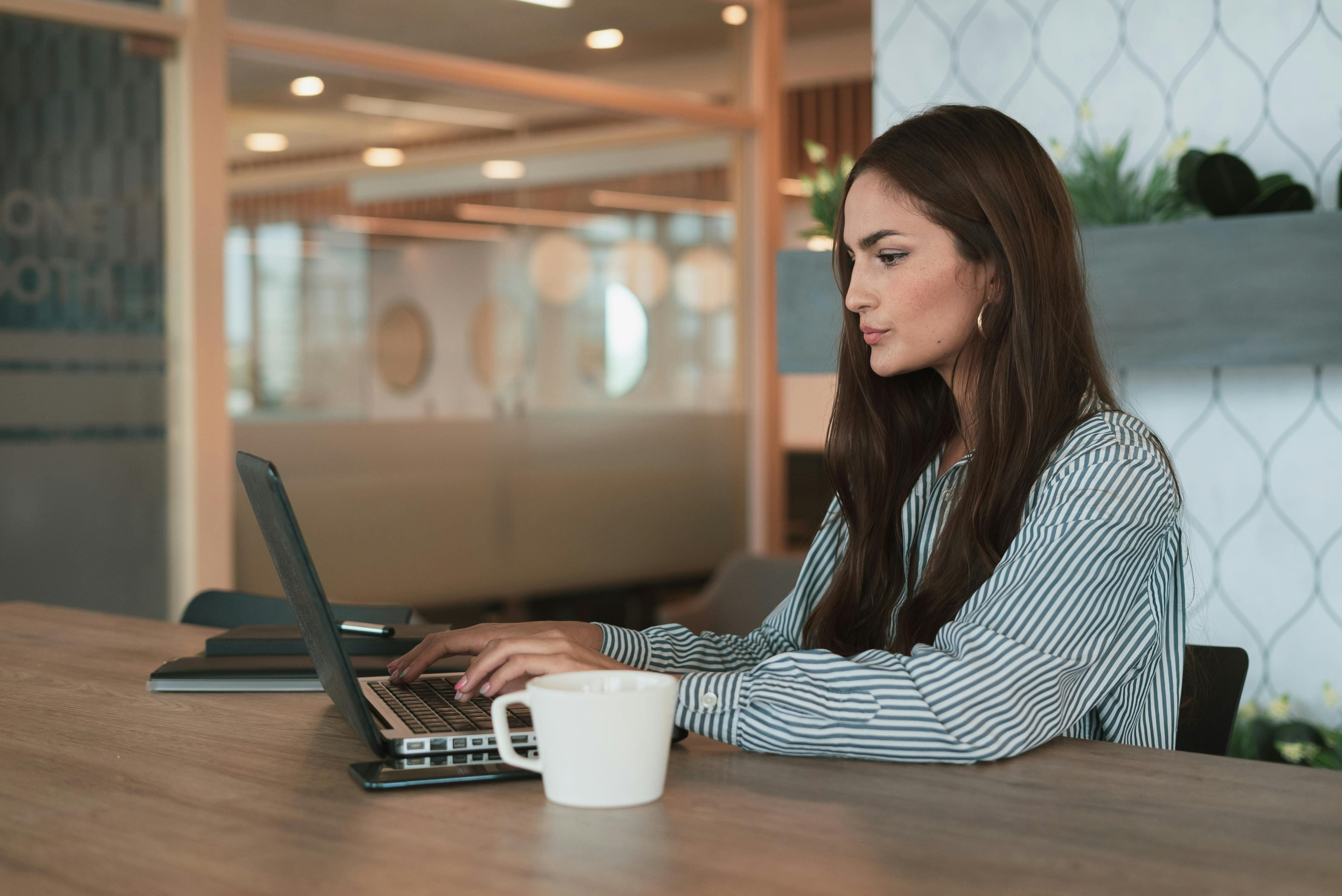 een vrouwelijke ondernemer, aan het werk achter haar laptop met een kop koffie.