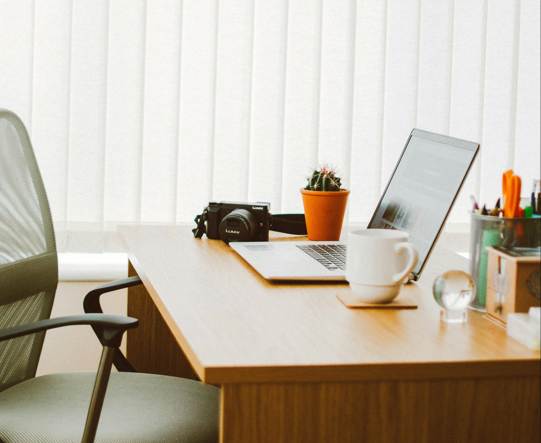 een bureau met een laptop, kop koffie en fotocamera